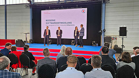 Vier Personen stehen auf einer Bühne und halten einen Vortrag zum Thema moderne Softwareentwicklung
