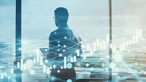 Eine Person in Geschäftskleidung steht mit einem Tablet vor einem großen Fenster und blickt nach draußen. Überlagert werden digitale Grafiken von Finanzdiagrammen und Datenzeilen, die Finanzen, Analytik oder Geschäftsstrategien symbolisieren.